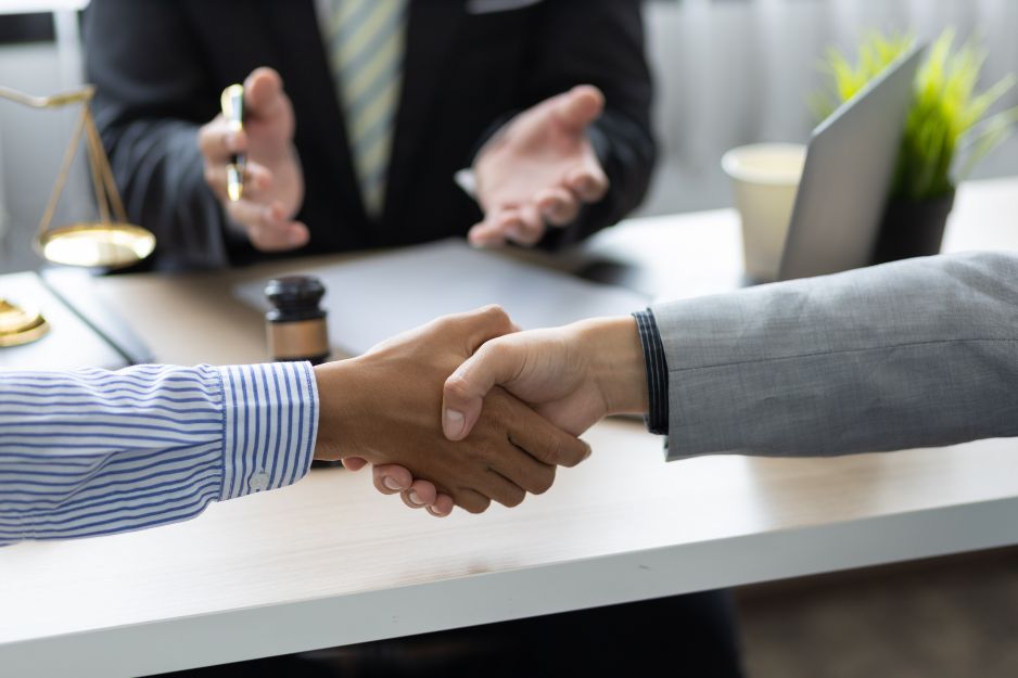 Two business professionals shaking hands at a table, symbolizing partnership and collaboration in legal support services.