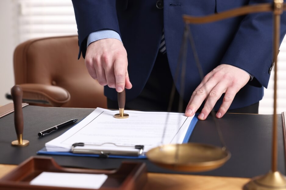 Professional notarizing a document beside scales of justice.