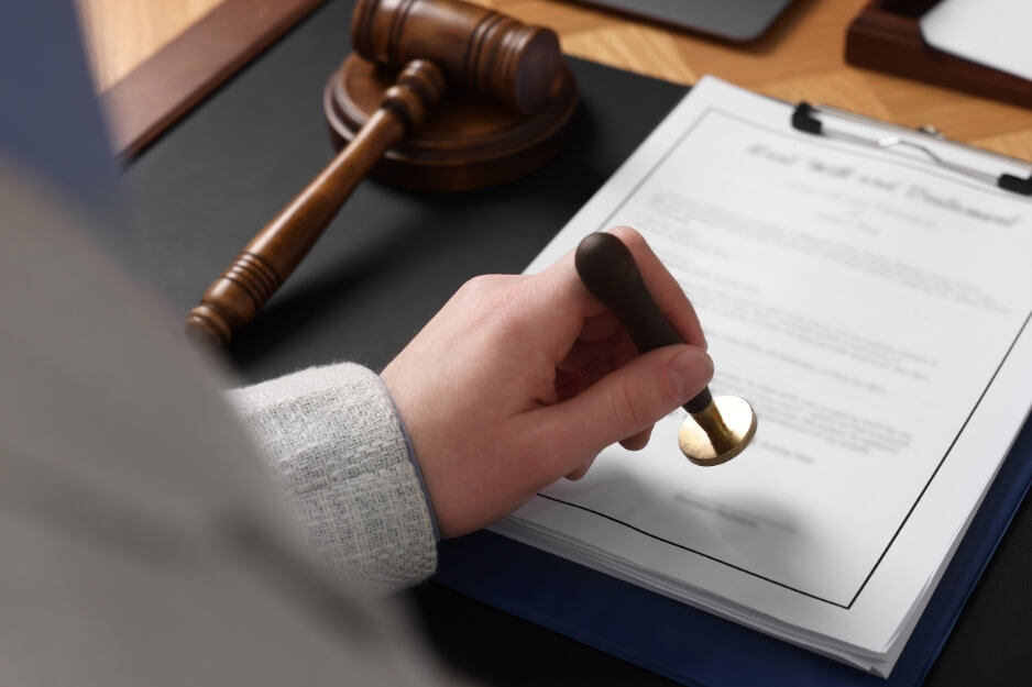 Hand holding notary stamp over final will document with gavel in background.