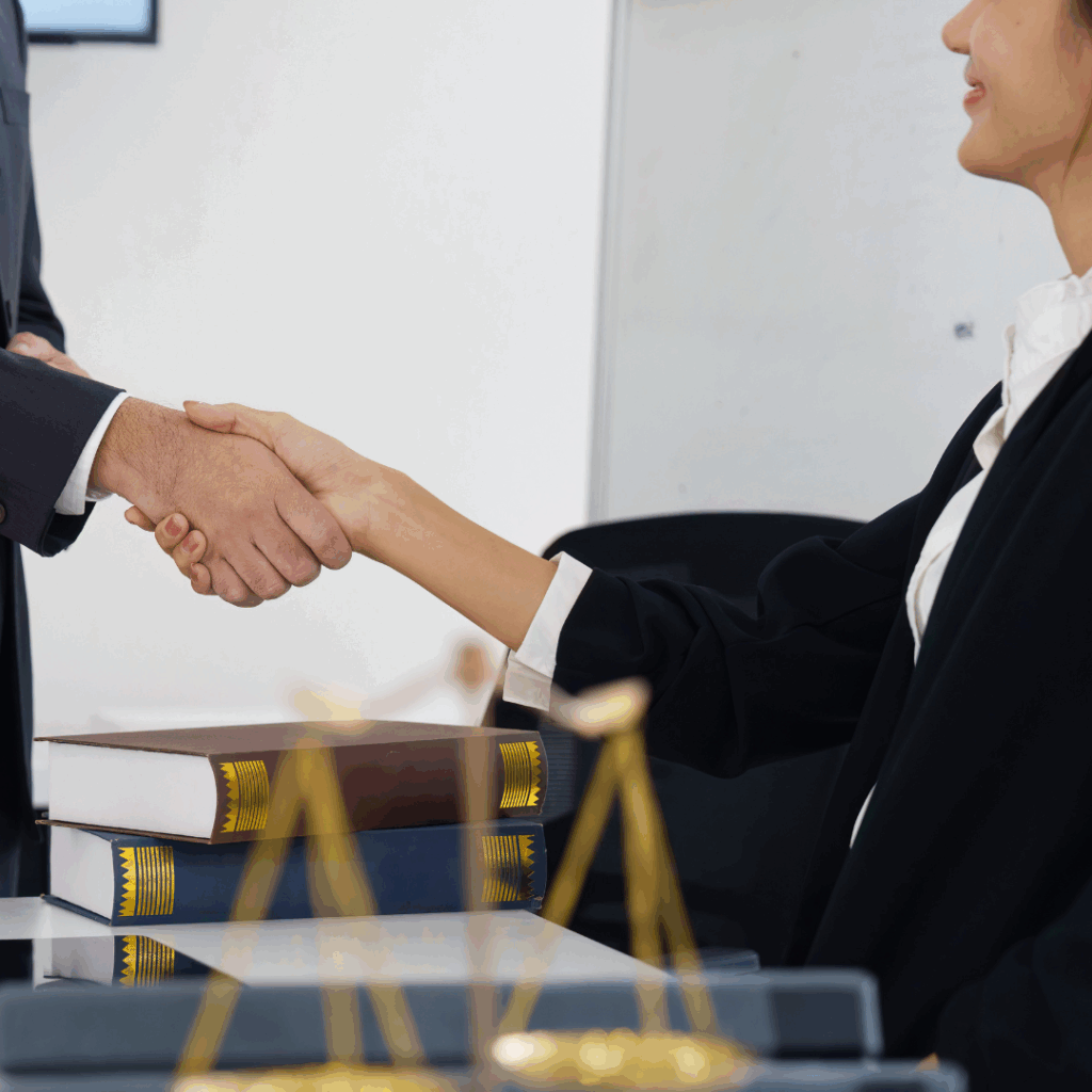 Legal professional and client shaking hands across a desk with law books and justice scale in view